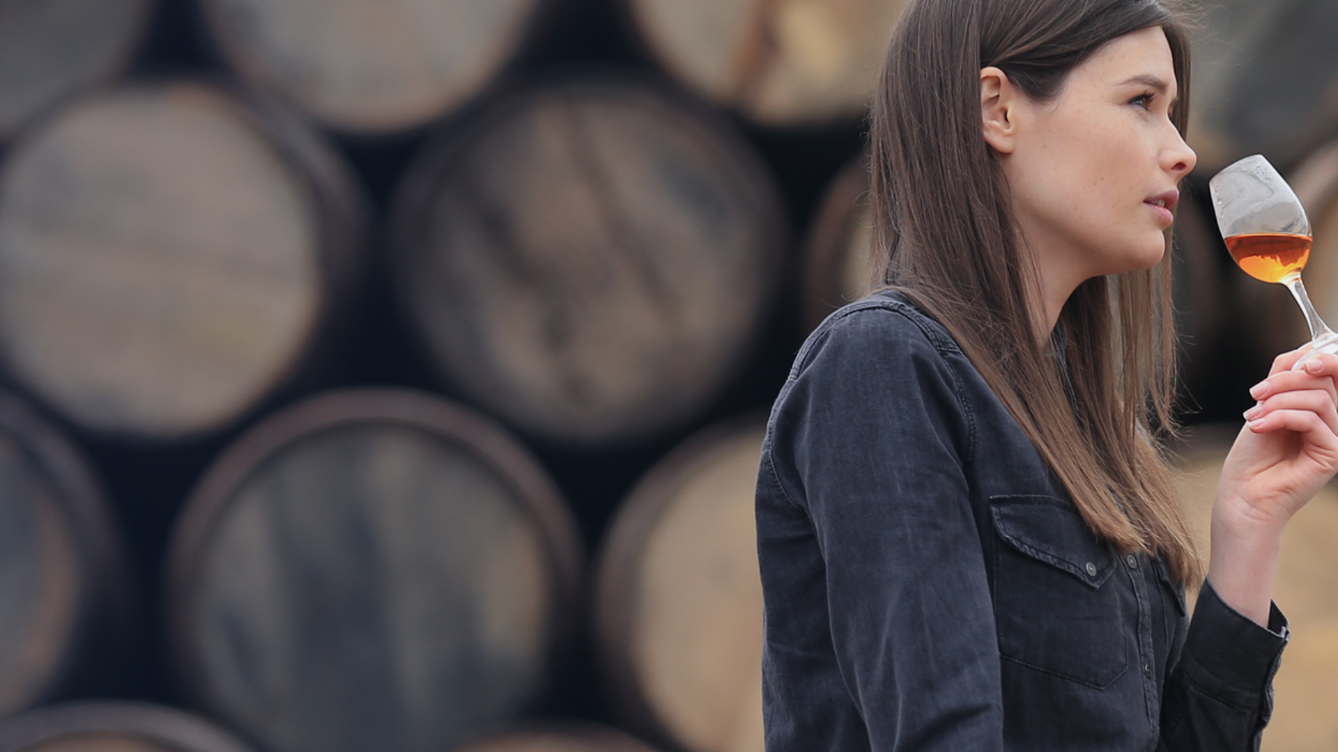 Woman standing in front of whisky barrels drinking a shot of whisky