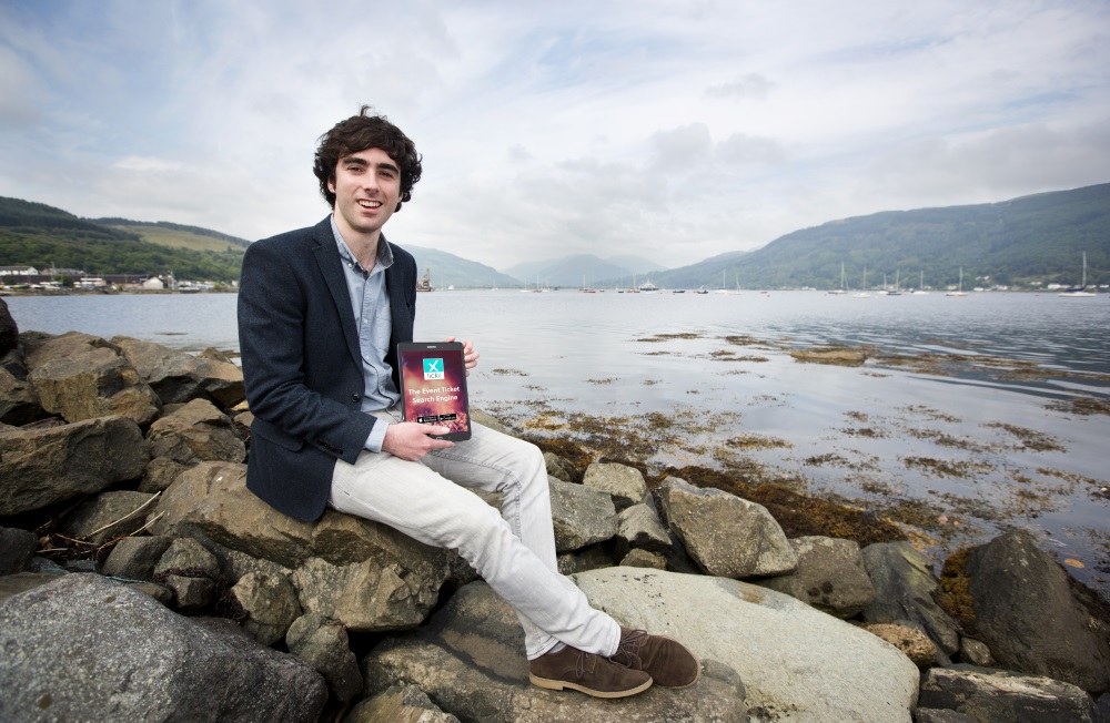 Sam Coley from technology company SAMTEQ sits on stoney shoreline holding award trophy award