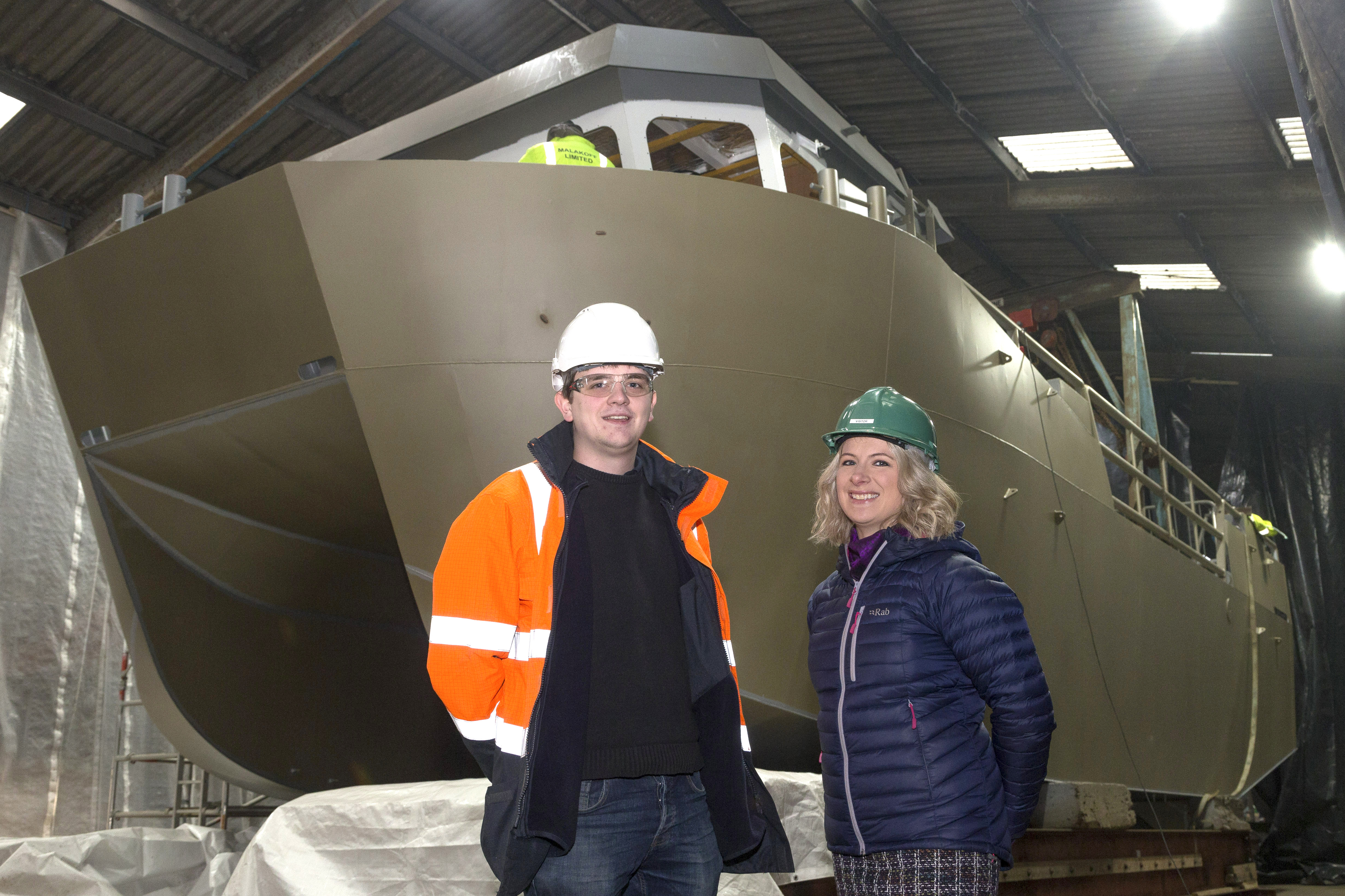 Two people standing in front of boat being constructed at Malakoff Limited, Shetland