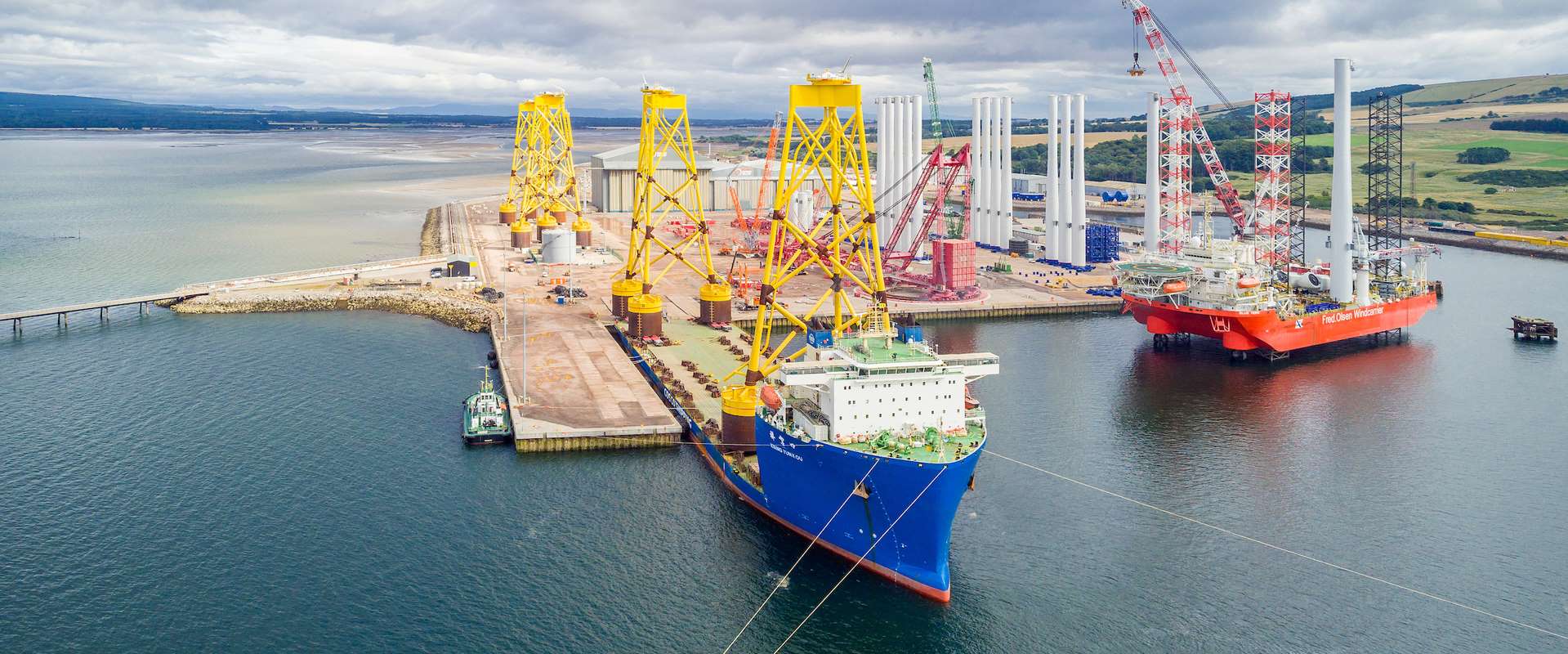 Large blue tanker docked at Cromarty with huge yellow and red offshore wind structures in the background.